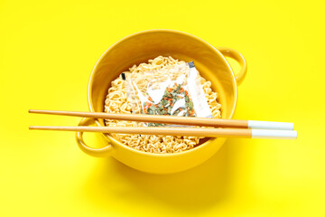 Bowl with raw instant noodles, condiment and wooden chopsticks on yellow background