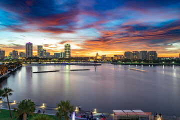Downtown St. Petersburg, Florida skyline at sunset with dramatic colorful clouds, waterfront buildings, palm trees, and reflections on the calm bay.