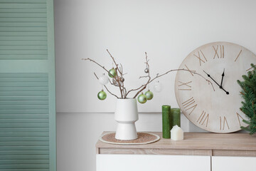 Vase with tree branches and Christmas baubles on chest of drawers in room