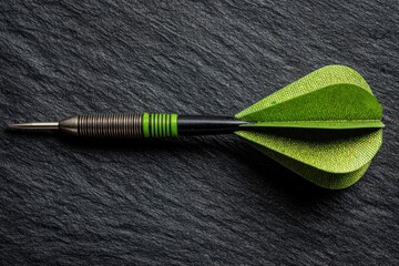 A dart with a metallic tip and green fletching laid on a textured black surface