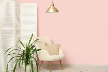 Hanging lamp, armchair, folding screen and houseplant near pink wall in room