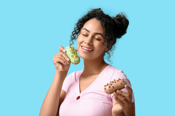 African-American woman with tasty eclairs on blue background