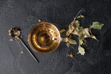 Cup of tasty linden tea with spoon on black background