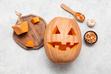 Wooden board with carved Halloween pumpkin, bowl of seeds, spoon and candle on white grunge...