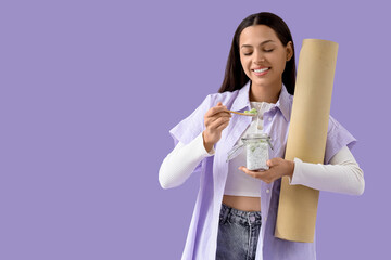 Young woman with chia seed pudding and fitness mat on lilac background