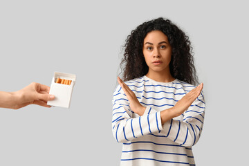Young African-American woman rejecting pack of cigarettes on grey background. Stop smoking concept