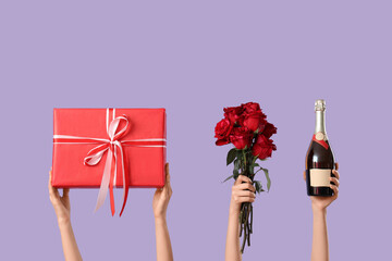Female hands with gift box, roses and bottle of champagne on lilac background. Valentine's day...