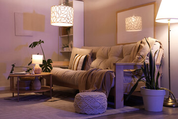 Interior of living room with comfortable sofa, coffee table and glowing lamps at night