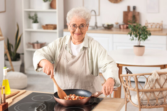 Fototapeta Senior woman frying vegetables in kitchen