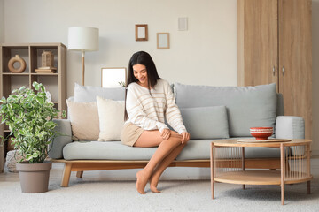 Young woman putting on beige tights at home