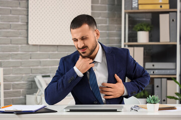Young businessman suffering from chest pain at table in office