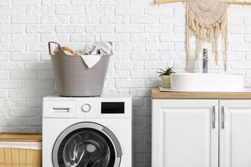 Modern washing machine, laundry baskets and chest of drawers with sink in bathroom