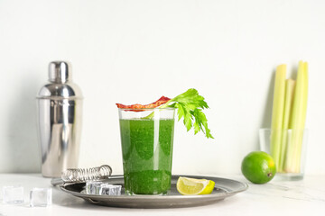Glass of green bloody mary cocktail with bacon, celery and lime on white background