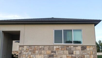 フラット屋根と大きなガラスパネルを備えた現代的な平屋住宅。ベージュと石材の外観が柔らかな日差しの下で調和する洗練された建築デザイン

