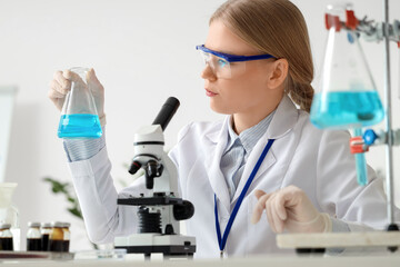 Female scientist with flask and microscope working in laboratory