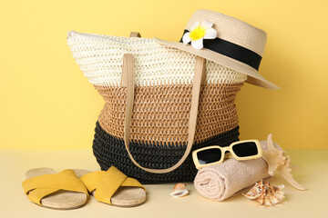 Wicker bag, seashells and beach accessories on yellow background, closeup