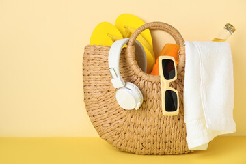 Wicker bag with headphones and beach accessories on yellow background, closeup