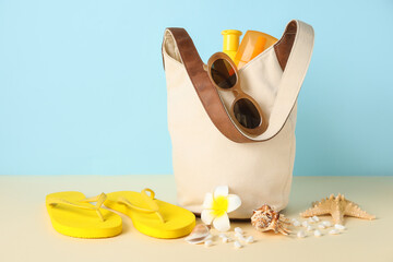 Bag with bottles of sunscreen cream and beach accessories on color background, closeup