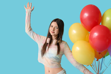 Beautiful teenage girl with colorful air balloons and headphones on blue background