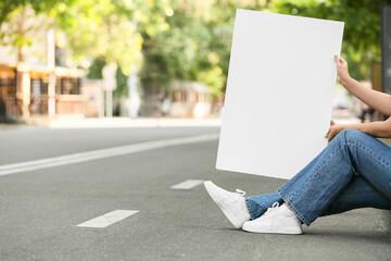 Young woman holding blank poster on city road