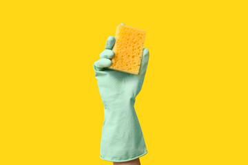 Hand in rubber glove holding sponge for cleaning on yellow background