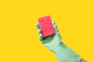 Hand in rubber glove holding sponge for cleaning on yellow background