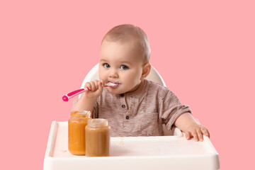 Cute little baby eating puree in high chair on pink background