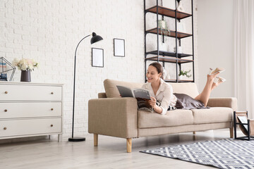 Young woman reading magazine while resting after work on couch at home