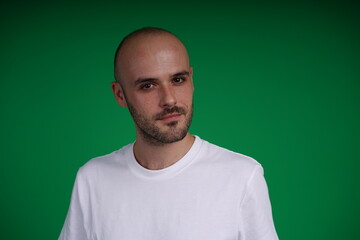Fototapeta premium Young man with a variety of emotions, wearing a white t-shirt standing against a green background. Studio shot with copy space.
