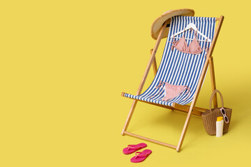 Deckchair with stylish swimsuit and beach accessories on yellow background, closeup