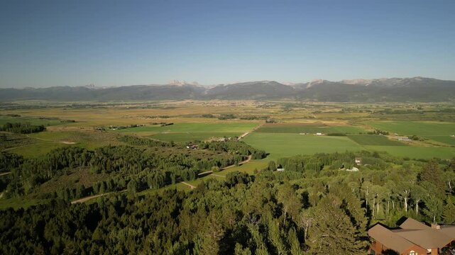 Aerial above forested mountain homes in Victor Idaho in summertime with view of Tetons