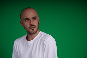 Fototapeta premium young man wearing a white t-shirt standing against a green background. Studio shot with copy space.