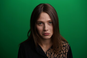 Obraz premium A young woman poses in a studio with a green background, showing natural emotions, full of expressions and dynamic movements. Unedited image