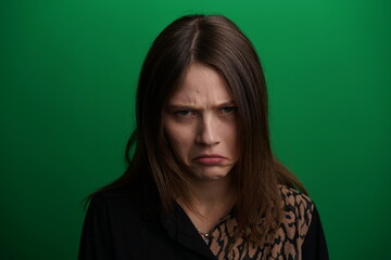 Fototapeta premium A young woman poses in a studio with a green background, showing natural emotions, full of expressions and dynamic movements. Unedited image