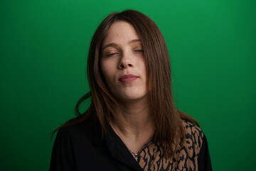 Fototapeta premium A young woman poses in a studio with a green background, showing natural emotions, full of expressions and dynamic movements. Unedited image