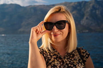 Closeup beautiful mid adult woman posing by holding sunglasses frame and looking at camera 