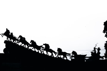 Dramatic silhouette of Krishna and Arjuna in a powerful chariot, pulled by horses against a bright sky, depicting an iconic Hindu epic scene.