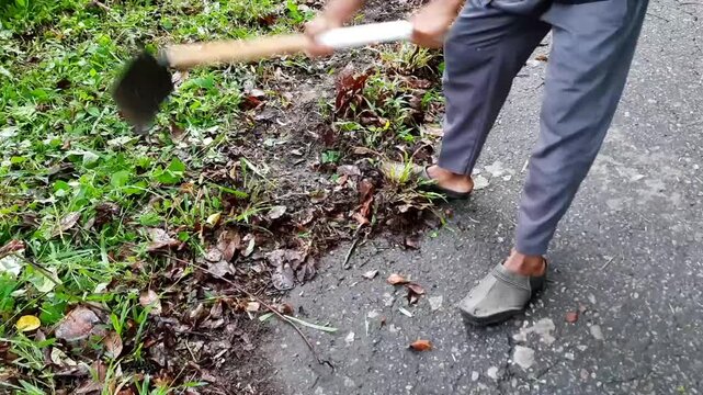 a man cleaning the edge of an asphalt road using a hoe. clearing soil and grass covering the roadside