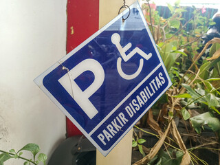 Handicap parking indication sign, blue and white, hanging outdoors in a natural and somewhat...