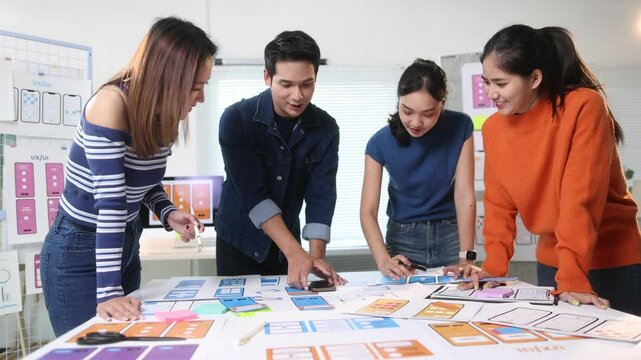 Young mobile app designers are collaborating on user interface and user experience layouts for a new mobile application, discussing and reviewing design elements.