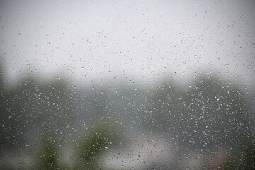 Raindrops on a window obscure the tranquil view of a misty landscape.