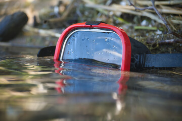 Red and black diving mask partially submerged in clear water with droplets.