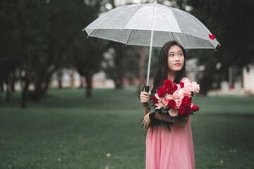 Young Woman Holding Flowers and Umbrella in Rainy Park Atmosphere