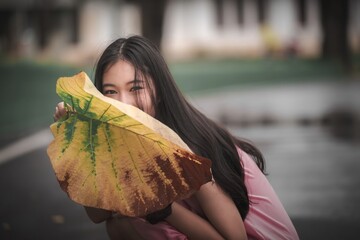 Young Woman Playfully Hiding Behind Large Leaf in Natural Setting