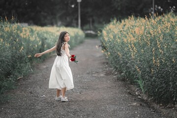 Young Girl in White Dress Holding Roses on Flower Pathway