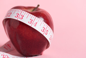 Red apple and a pink measuring tape on a pink background, healthy eating and weight management.