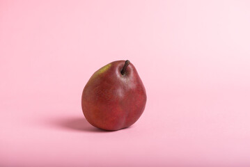 A single, ripe red pear rests on a pale pink background.