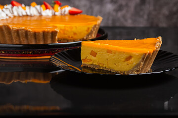 A mango tart, adorned with whipped cream, fresh strawberries, and a delicate chocolate drizzle.