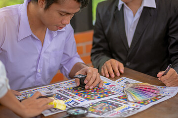 Team graphic designer checking print quality of media graphics proof print and color guides in printing industry. Selected focus