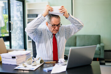 Senior businessman rips paperwork in rage at office desk. Workplace stress, anger, chaos, and...